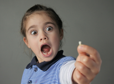 Little girl who just lost a tooth holding it out in front of her.